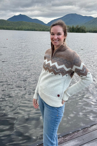 Woman wearing a patterned sweater by a lake with mountains in the background