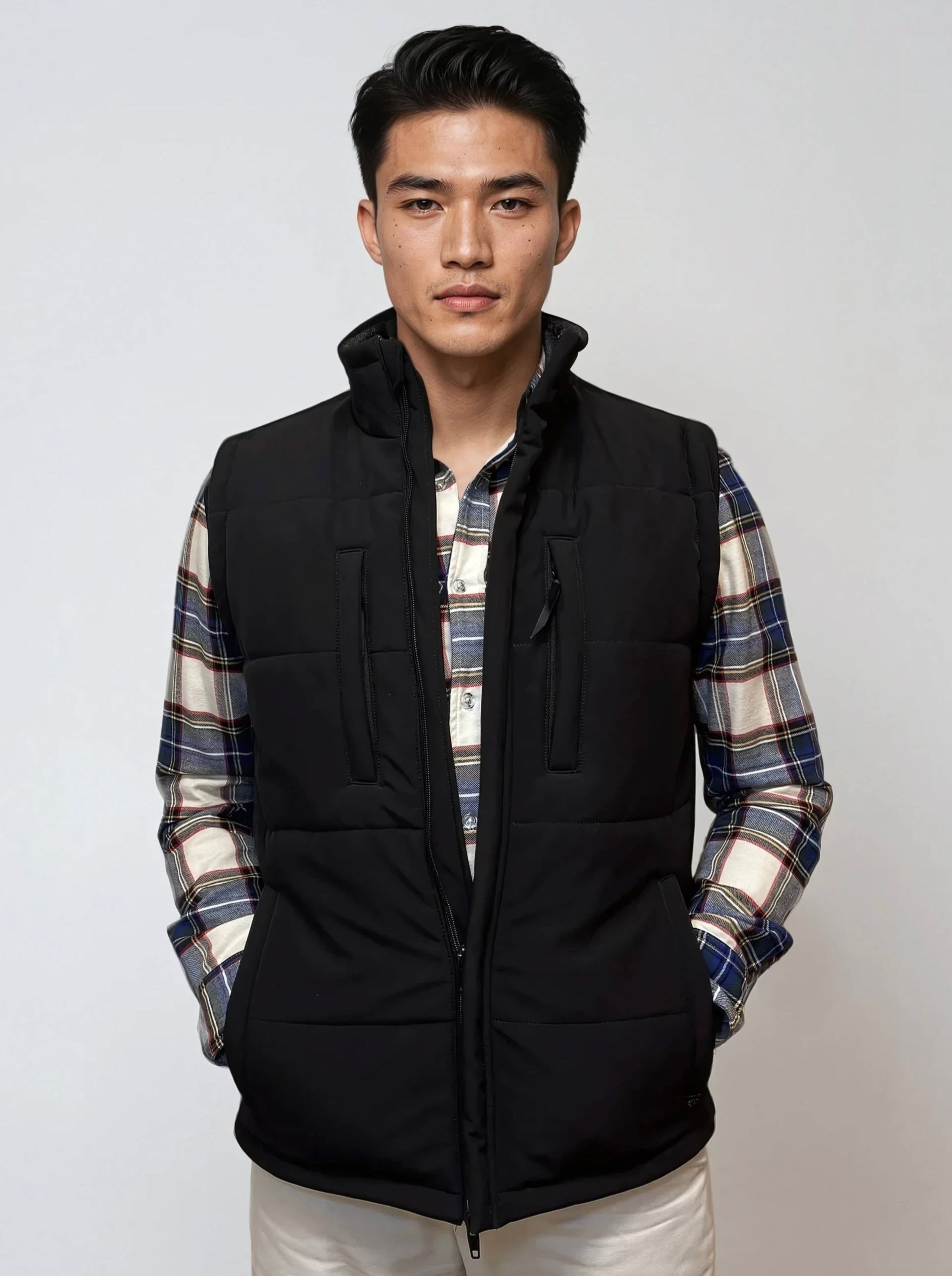 Man wearing a black vest over a plaid shirt on a white background